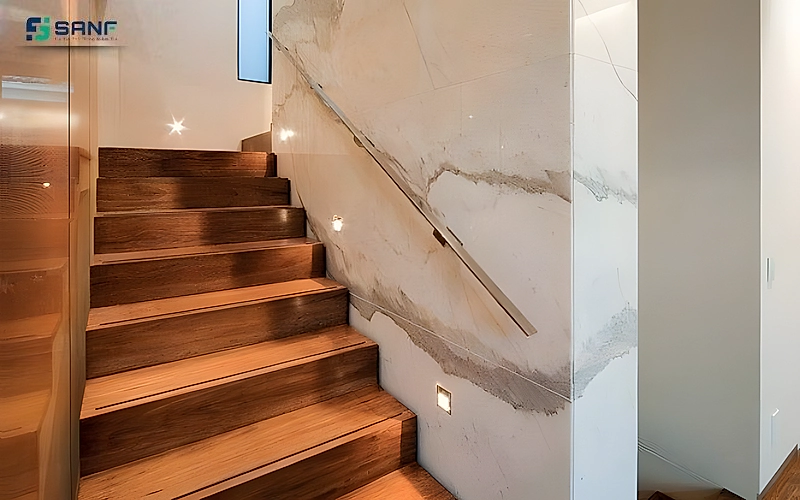 Vách vân đá marble trắng gân vàng kem cạnh cầu thang bậc gỗ nâu có đèn âm bậc