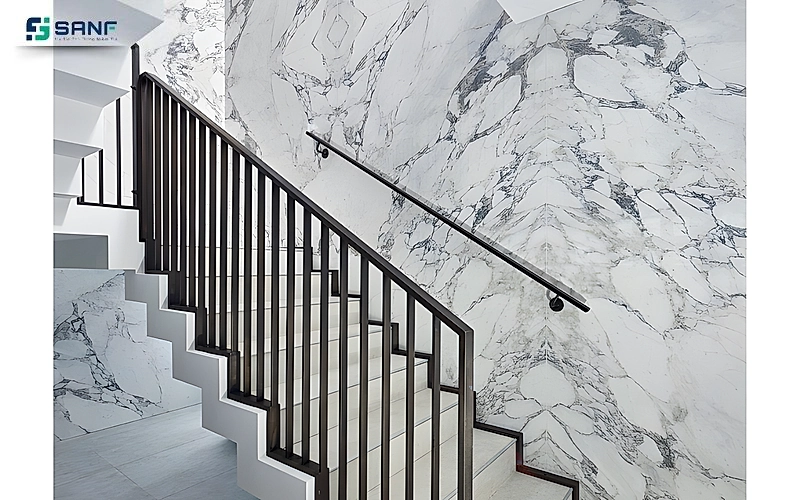 Vách vân đá marble trắng gân xám đậm cạnh cầu thang lan can sắt đen và tay vịn gắn tường