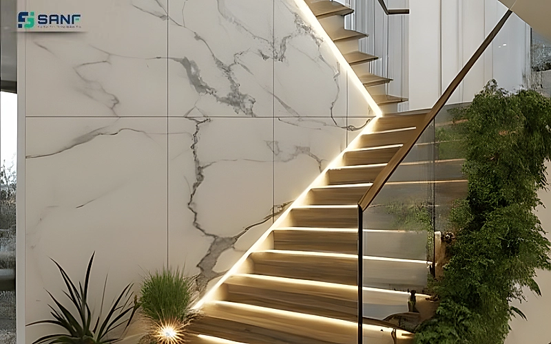 Vách vân đá trắng gân xám lớn cạnh cầu thang có đèn led viền bậc lan can kính và cây xanh