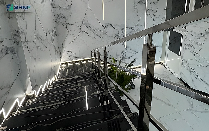 Hành lang cầu thang vách vân đá trắng gân xám sàn đá đen và lan can inox bóng
