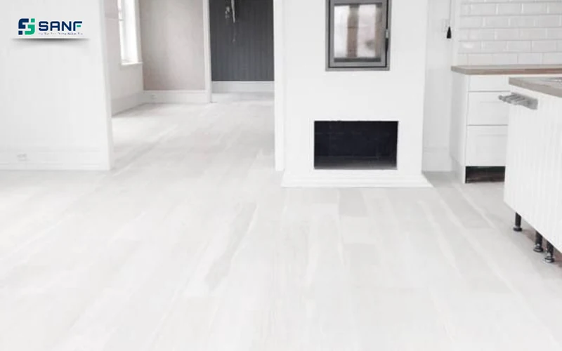 Không gian mở lát sàn nhựa giả gỗ trắng cạnh lò sưởi và tủ bếp trắng