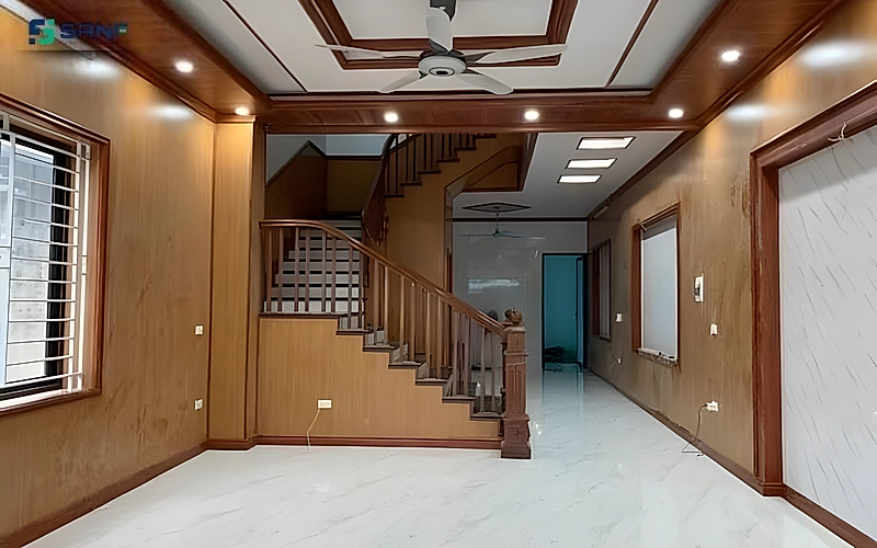 Phòng khách nhà phố ốp tấm vân gỗ nâu cam quanh cầu thang gỗ trên sàn gạch trắng