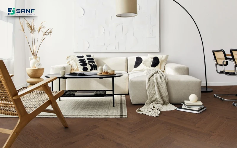 Phòng khách lát sàn nhựa vân óc chó kiểu xương cá phối tường trắng sofa kem và ghế mây