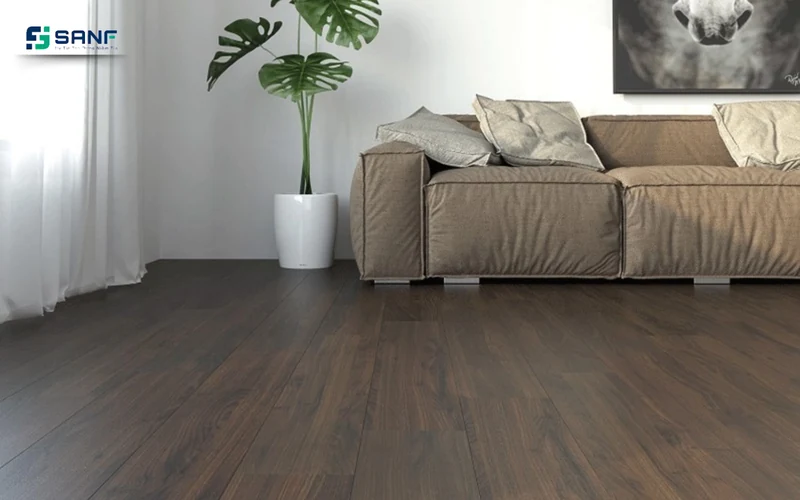 Phòng khách lát sàn nhựa giả gỗ óc chó đậm kết hợp tường trắng sofa nâu be và chậu cây xanh