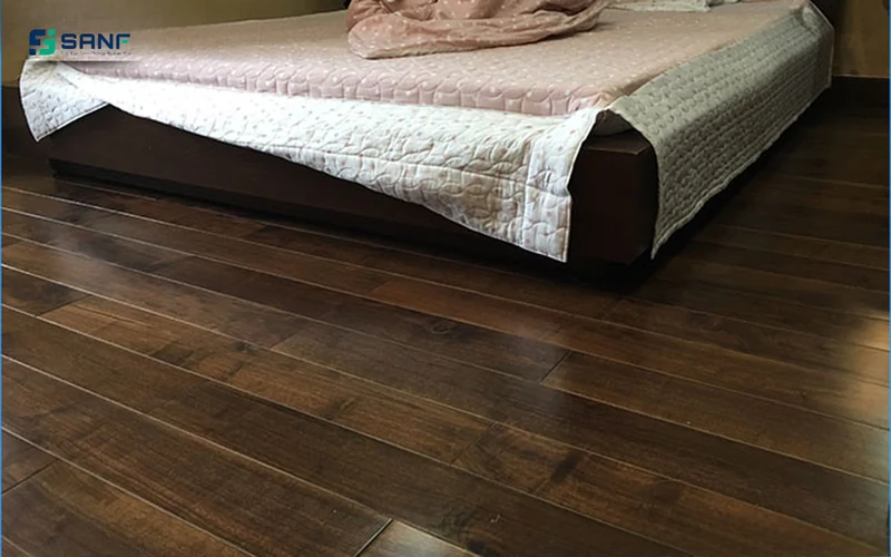 Phòng ngủ lát sàn nhựa vân óc chó nâu trầm bóng nhẹ dưới giường thấp phủ ga trắng