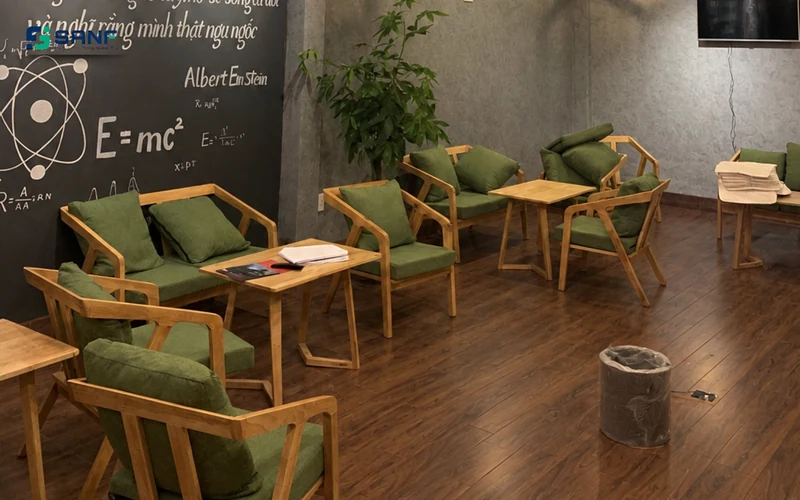 Quán cà phê lát sàn nhựa vân óc chó đậm với bàn ghế gỗ đệm xanh rêu và tường bảng đen