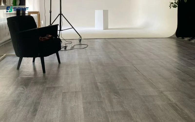Studio chụp ảnh phông nền trắng với sàn nhựa giả gỗ tông xám và ghế bành đen