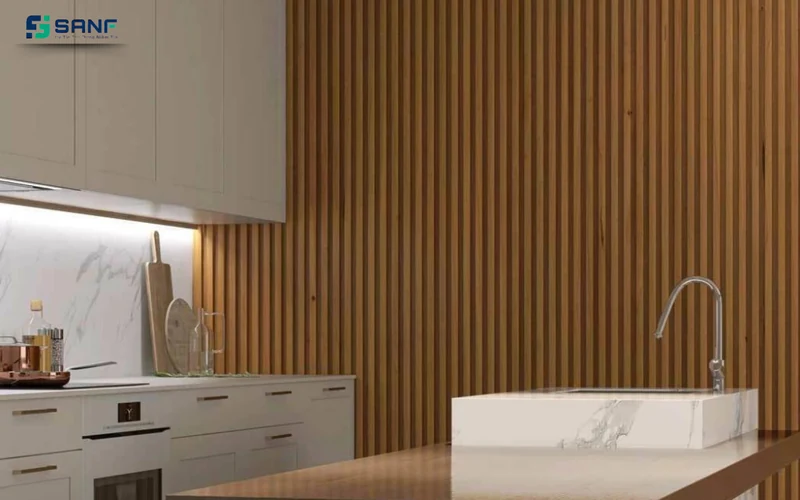 Góc bếp có mảng tường lam gỗ nâu cạnh đảo bếp mặt đá trắng và vòi nước